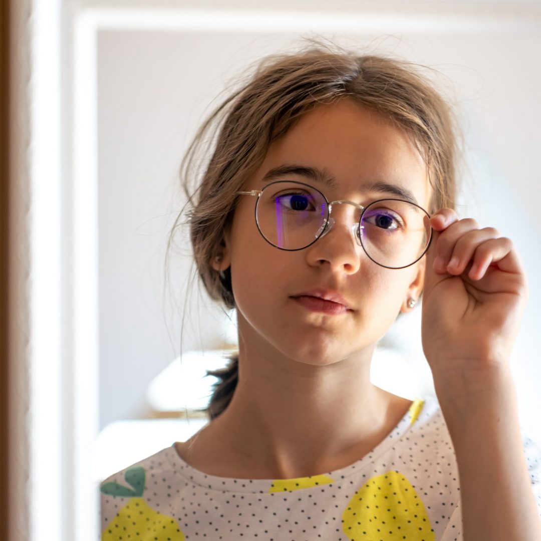 Sleepy teen girl in glasses looks at herself in the mirror in the morning, the concept of self-acceptance.